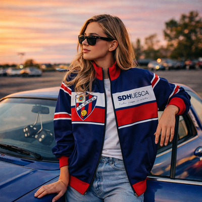 Woman in a colorful jacket leaning against a car at sunset