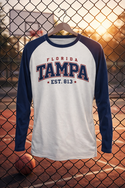 Long-sleeve shirt with 'Florida Tampa EST. 813' text on a hanger against a chain-link fence background.
