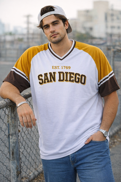 Man wearing a 'San Diego' jersey leaning against a fence with a cityscape background