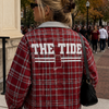 Person wearing a red plaid jacket with 'THE TIDE' on it, standing outdoors.