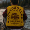 Person wearing an 'Offroad Club' vest sitting by a campfire with mountains in the background