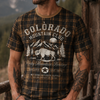 Man wearing a 'Colorado Mountain Club' t-shirt standing on a wooden deck with mountains in the background
