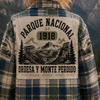 Person wearing a plaid jacket with a national park design, standing in a mountainous landscape.
