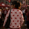 Person wearing a sweater with red elephant patterns at a sports event, surrounded by people and tents.