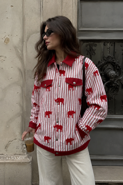 Woman wearing a red and white patterned shirt with a bear design, standing against a textured wall.