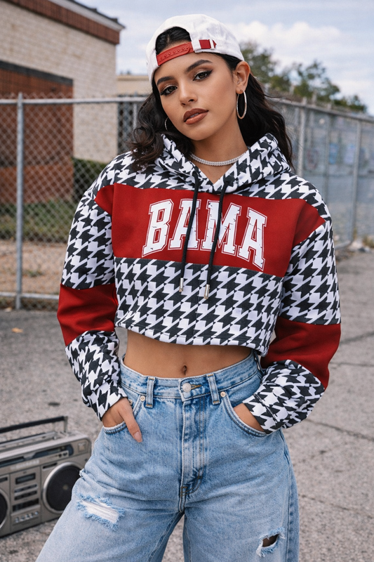 Person wearing a houndstooth pattern hoodie with 'Bama' text, blue jeans, and a cap, standing outdoors.