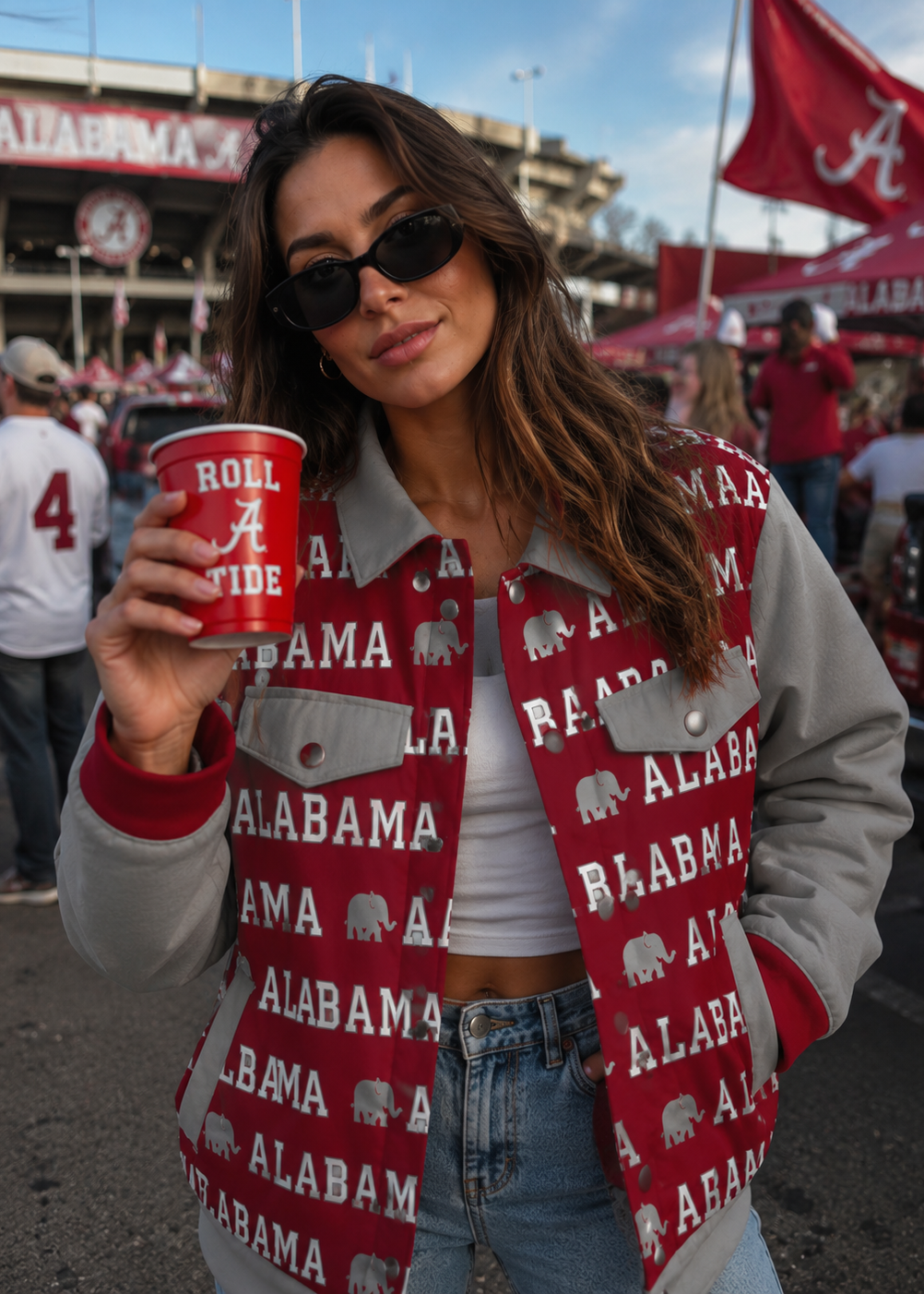Woman wearing an Alabama-themed jacket and holding a red cup at a sports event.