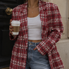Woman wearing a red plaid shirt, white top, and blue jeans, holding a coffee cup, standing in front of a building.