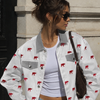 Woman wearing a white jacket with red patterns, white top, and blue jeans standing against a building.