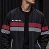 Man wearing a black jacket with red and gray stripes and 'Alabama' branding, standing against a dark wall.