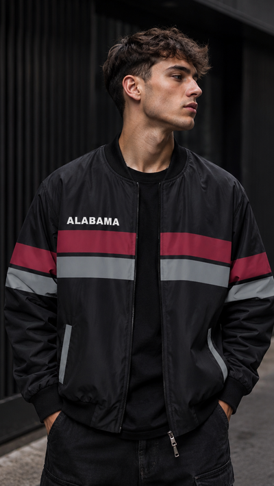 Man wearing a black jacket with red and gray stripes and 'Alabama' branding, standing against a dark wall.