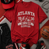 Red t-shirt with 'Atlanta 1936' design, black shorts, red and black sneakers, and basketball on a sports-themed background.