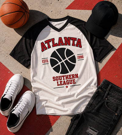 White t-shirt with basketball design and text, surrounded by a basketball, black cap, and white sneakers on a red and gray surface.