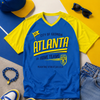 Blue and yellow t-shirt with 'Atlanta' text, surrounded by accessories on a colorful background