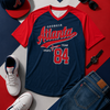 Navy and red sports-themed t-shirt with 'Georgia Atlanta Team Sports 84' text, surrounded by casual clothing and accessories on a colorful background.