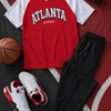 Red and white 'Atlanta Georgia' jersey with black pants, white sneakers, and a basketball on a sports court.