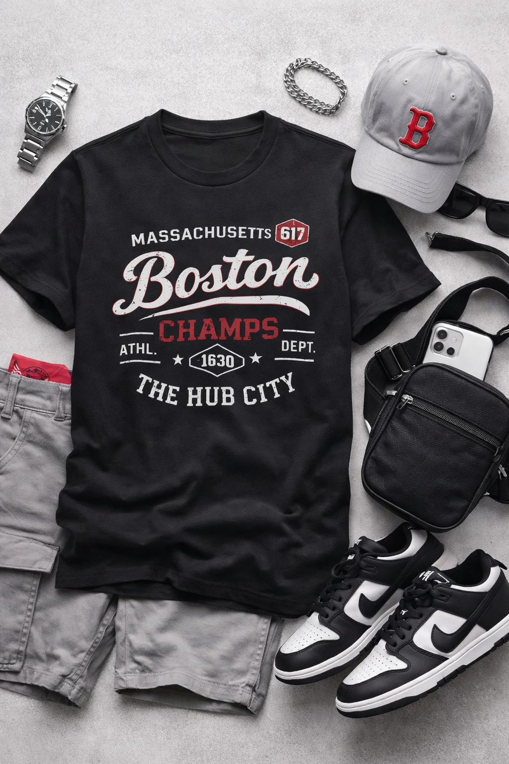 Black t-shirt with 'Boston Champs' text, surrounded by casual clothing and accessories on a gray surface.