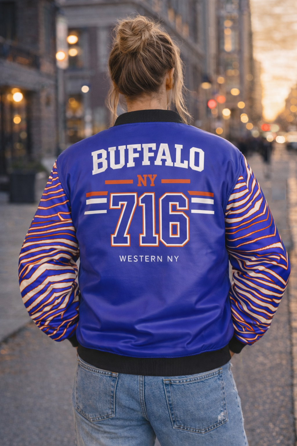 Person wearing a blue and orange varsity jacket with 'Buffalo NY 716' on the back, standing in an urban setting.