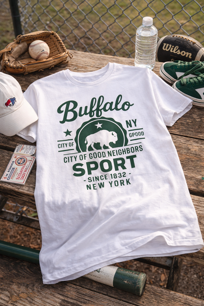 White t-shirt with 'Buffalo NY' graphic on a wooden table with sports equipment.