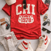 Red t-shirt with 'CHI Athletics 1978' design, white sneakers, cap, socks, and accessories on a gray surface.