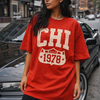 Woman wearing a red 'CHI 1978' t-shirt standing on a city street.