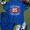 Blue 'Chicago College 85' t-shirt with shorts, sneakers, headphones, and a football on grass.