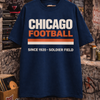 Navy blue t-shirt with 'Chicago Football' text on a hanger against a graffiti-covered wall.
