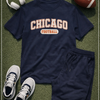 Navy blue t-shirt with 'Chicago Football' text, navy shorts, white sneakers, headphones, and football on a green surface.