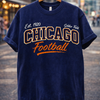 Navy blue t-shirt with 'Chicago Football' text on a hanger against a city street background