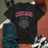 Black t-shirt with 'Chicago Illinois 23' design, blue pants, white sneakers, and basketball on a sports court.