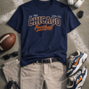 Navy blue t-shirt with 'Chicago Football' text, beige shorts, sneakers, football, sunglasses, and headphones on a textured surface.