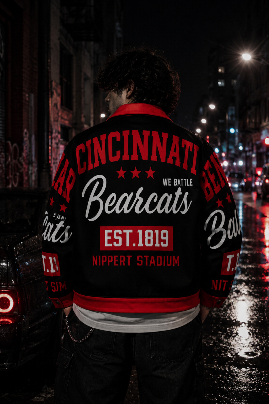 Person wearing a Cincinnati Bearcats jacket on a city street at night.