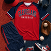 Cleveland baseball-themed outfit with jersey, cap, shorts, shoes, and sports equipment on a baseball field background.