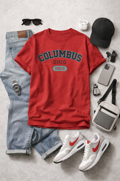 Red t-shirt with 'Columbus, Ohio 1812' design, jeans, sneakers, and accessories on a gray surface.