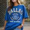 Woman wearing a blue 'DALLAS' t-shirt blowing bubble gum outdoors.