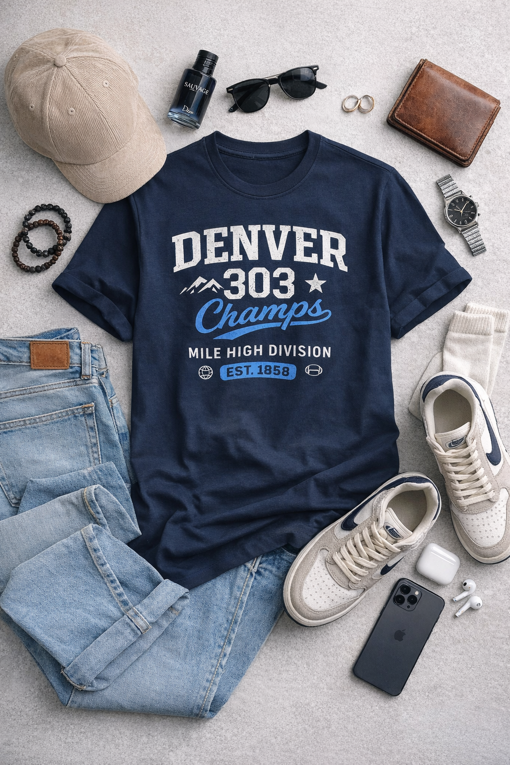 Navy blue t-shirt with 'Denver 303 Champs' text, surrounded by casual items on a light gray surface.