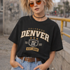 Person wearing a black 'Colorado Denver' t-shirt with sunglasses and pigtails in an urban setting.