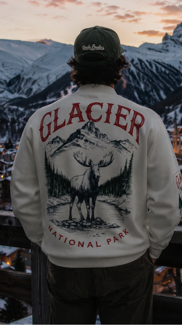 Person wearing a Glacier National Park sweatshirt overlooking a snowy mountain village at sunset.