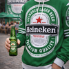 Person wearing a Heineken hoodie holding a bottle of Heineken beer.