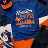 Blue t-shirt with 'Houston HOU713 SPACE CITY' design, surrounded by accessories on a colorful background