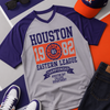Gray and purple t-shirt with 'Houston' text, sunglasses, cap, and jeans on a colorful background