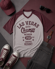 T-shirt with 'Las Vegas City Champs' design, surrounded by a cap, sunglasses, shoes, and watch on a patterned surface.