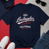 Navy blue t-shirt with 'Los Angeles Baseball Club' text, surrounded by a cap, sunglasses, and sneakers on a red and gray background.