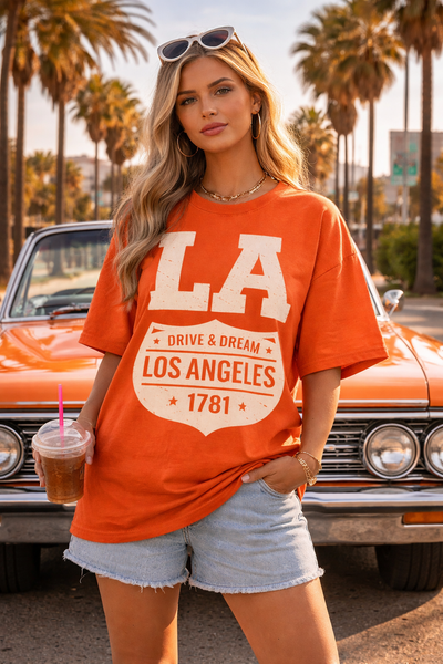 Woman wearing an orange 'Los Angeles' t-shirt in front of a classic car with palm trees in the background.