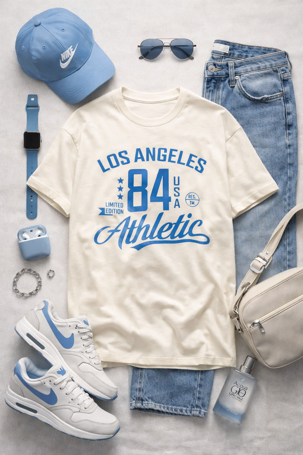 White t-shirt with 'Los Angeles 84 Athletic' design, blue cap, jeans, sneakers, and accessories on a light gray background.