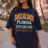 Person wearing a navy blue t-shirt with 'Miami Florida' text, standing on a beach boardwalk.
