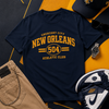 Navy t-shirt with 'New Orleans' text, cap, watch, pants, and sneakers on a geometric patterned background