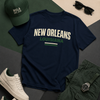 Navy blue t-shirt with 'New Orleans Louisiana' text, green cap, sunglasses, white sneakers, and green shorts on a geometric patterned surface.