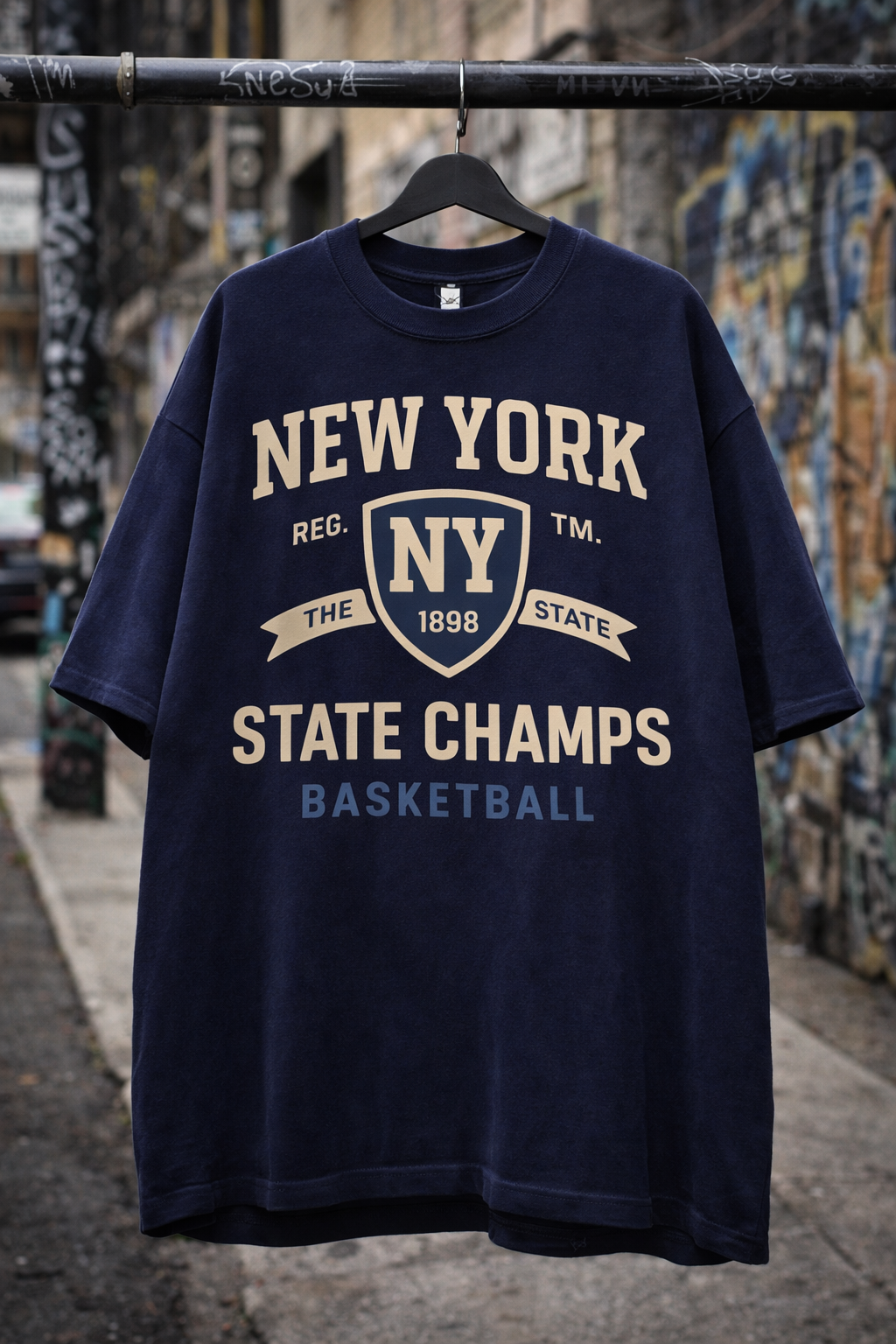 Navy blue t-shirt with 'New York State Champs Basketball' text on a hanger against a textured wall.