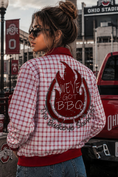 Person wearing a red and white checkered jacket with a graphic design, standing in front of a red truck and Ohio Stadium.